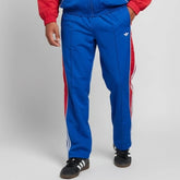 Blue tracksuit with red stripes worn by a person on a gray background